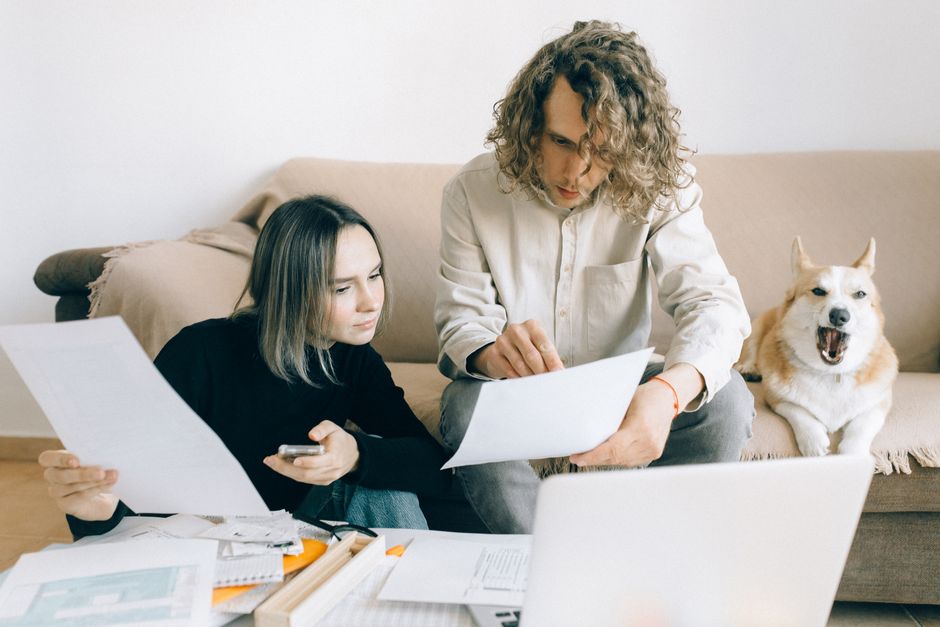 A couple working remotely at home with documents and a dog on the sofa.