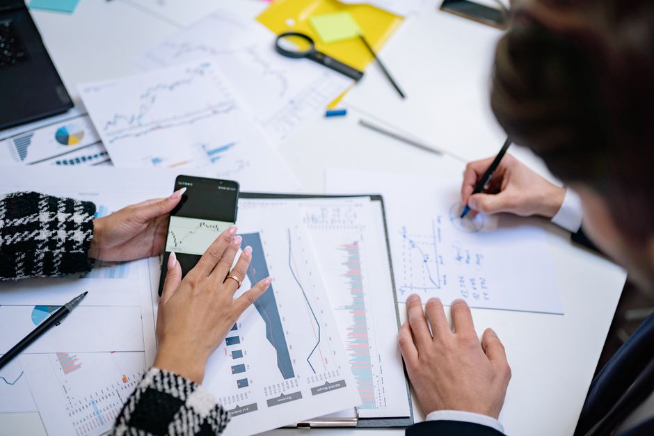 Overhead view of people analyzing financial graphs and data with smartphone and documents.