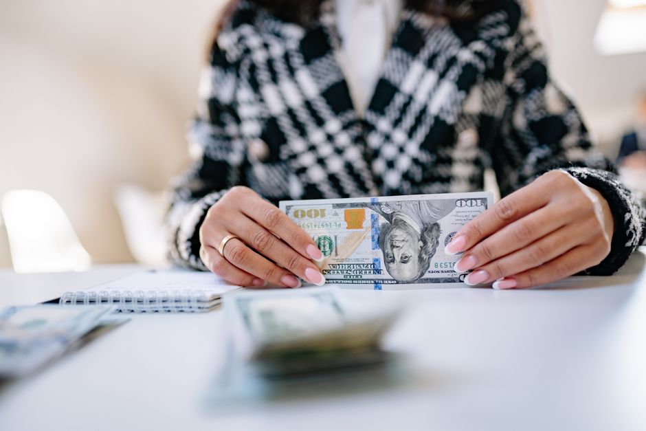 Close-up image of hands holding a US hundred dollar bill on a desk.