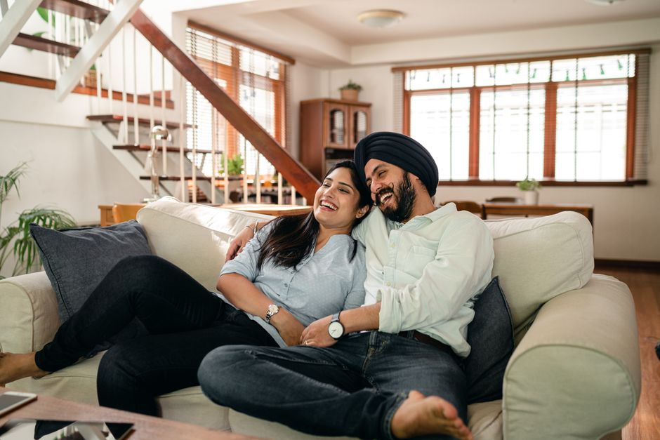 Relaxed young Indian couple in casual clothes spending lazy day together on couch and watching funny movie on TV