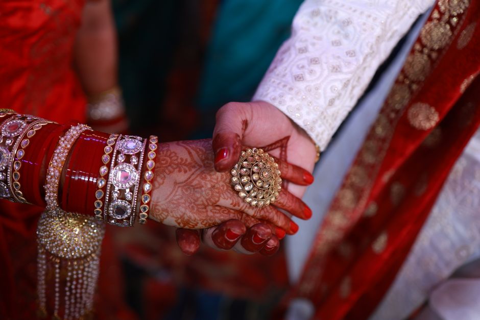 Close-up of hands in an Indian wedding showing intricate mehndi and jewelry.